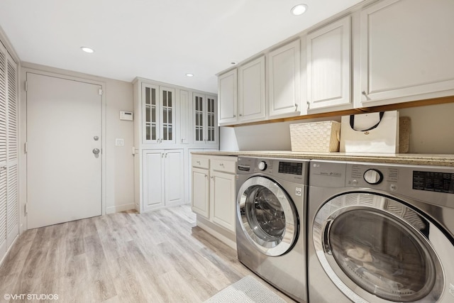 clothes washing area featuring cabinets, light hardwood / wood-style floors, and washing machine and dryer