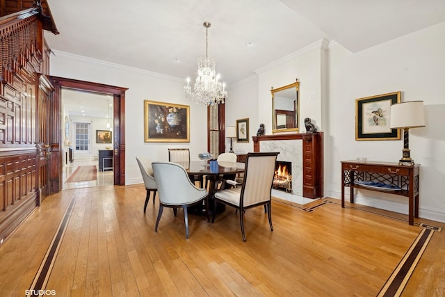 dining room featuring ornamental molding, light wood-type flooring, an inviting chandelier, and a fireplace