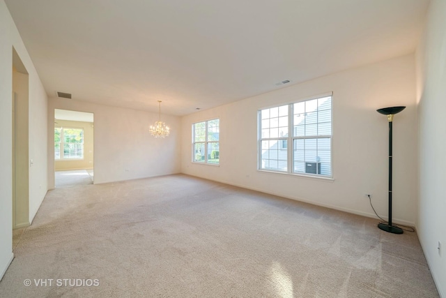 empty room with plenty of natural light, light carpet, and a chandelier