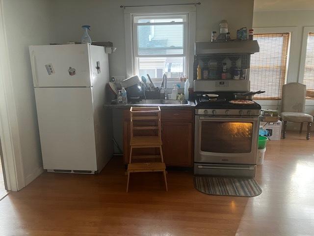 kitchen with white refrigerator, light hardwood / wood-style floors, stainless steel gas range oven, and sink