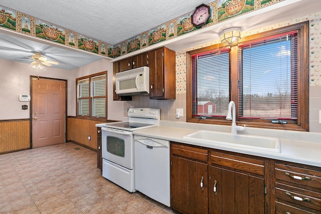 kitchen featuring white appliances, a wainscoted wall, light countertops, a textured ceiling, and a sink