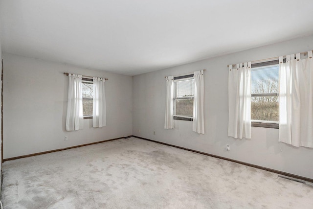 carpeted spare room featuring a healthy amount of sunlight, baseboards, and visible vents