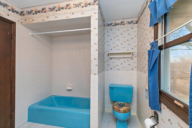 bathroom featuring toilet, tile walls,  shower combination, wainscoting, and wallpapered walls