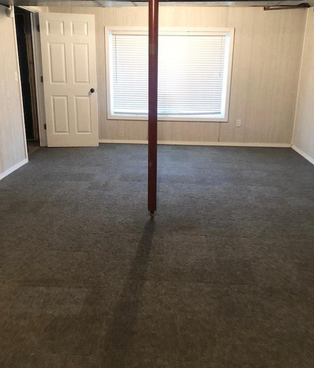 unfurnished room featuring plenty of natural light, dark carpet, and baseboards