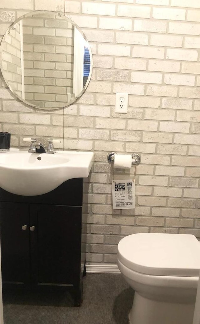 bathroom featuring brick wall, vanity, and toilet