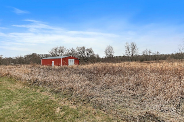 view of yard with a rural view, an outdoor structure, a detached garage, and an outbuilding