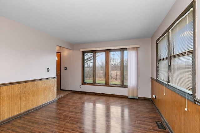 unfurnished room with baseboards, visible vents, wainscoting, wood finished floors, and wood walls