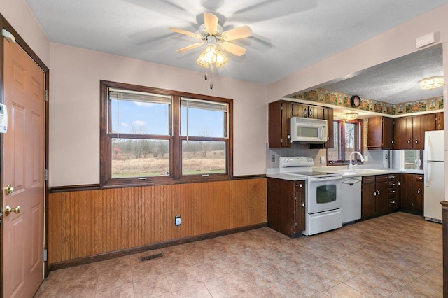 kitchen with a wainscoted wall, light countertops, white appliances, and a sink