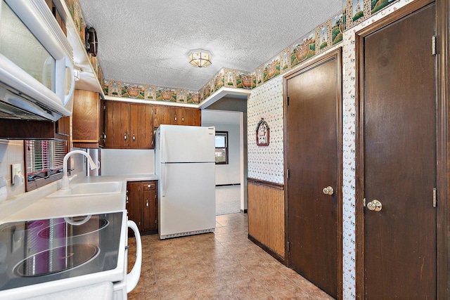 kitchen featuring a textured ceiling, white appliances, light countertops, wainscoting, and wallpapered walls