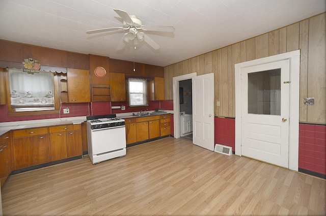 kitchen featuring wooden walls, light hardwood / wood-style flooring, ceiling fan, and white range with gas stovetop