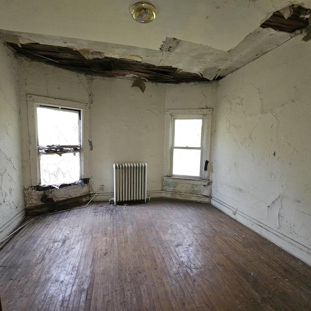 empty room featuring plenty of natural light, wood-type flooring, and radiator