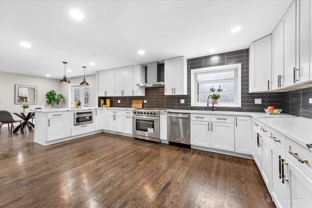 kitchen with decorative light fixtures, white cabinets, stainless steel appliances, and wall chimney range hood