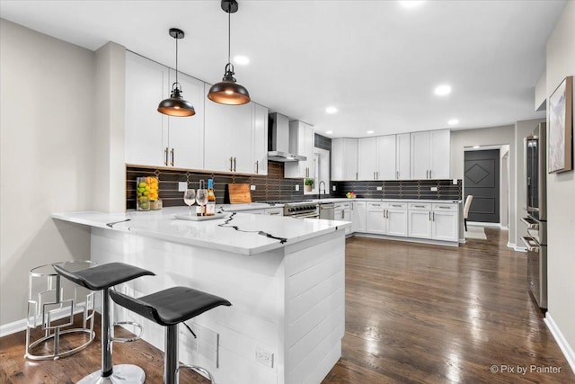 kitchen with kitchen peninsula, tasteful backsplash, wall chimney range hood, pendant lighting, and white cabinetry