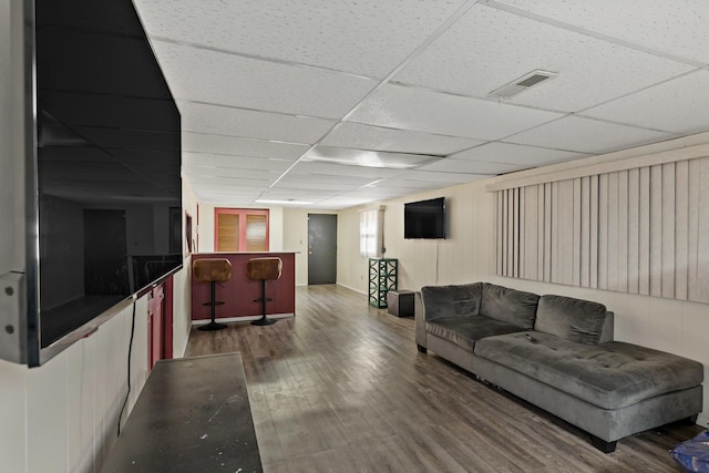 living room with a drop ceiling, hardwood / wood-style floors, and bar area