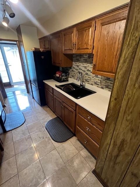 kitchen with black fridge, light tile patterned flooring, sink, and decorative backsplash