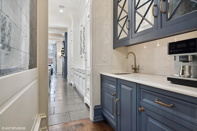 bar featuring dark wood-type flooring, blue cabinets, ornamental molding, and sink