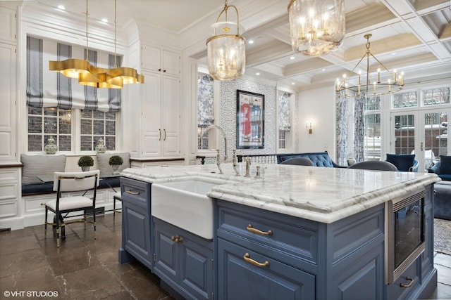 kitchen with stainless steel microwave, coffered ceiling, blue cabinets, decorative light fixtures, and a center island with sink