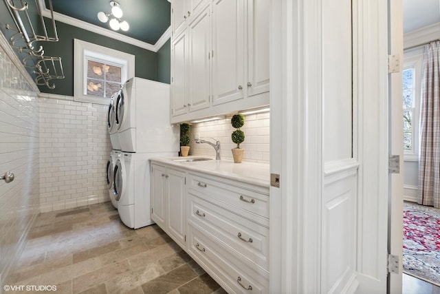 laundry area with cabinets, ornamental molding, sink, tile walls, and stacked washer and dryer