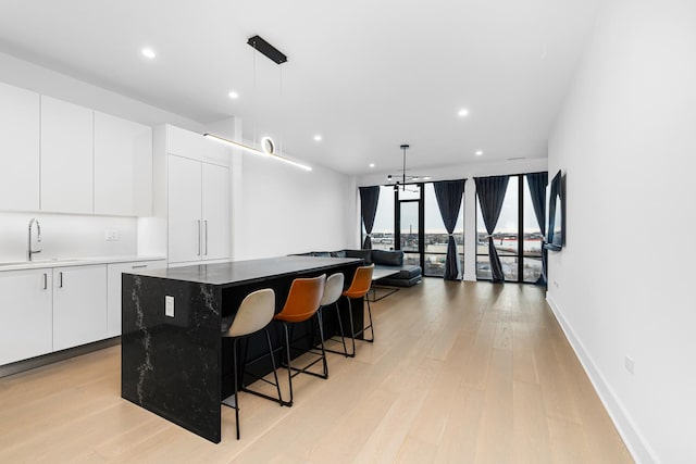 kitchen featuring floor to ceiling windows, a center island, sink, light hardwood / wood-style flooring, and white cabinets