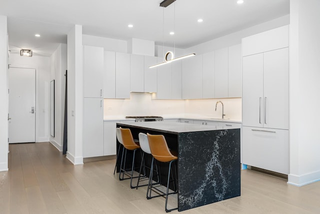 kitchen featuring sink, a kitchen island, light hardwood / wood-style flooring, decorative light fixtures, and white cabinets