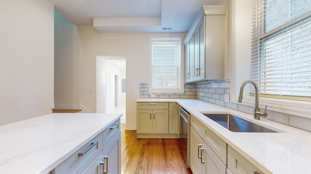 kitchen featuring tasteful backsplash, light stone counters, sink, dishwasher, and light hardwood / wood-style floors