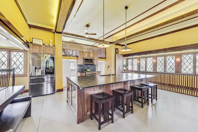 kitchen with a sink, appliances with stainless steel finishes, a large island, decorative backsplash, and dark countertops