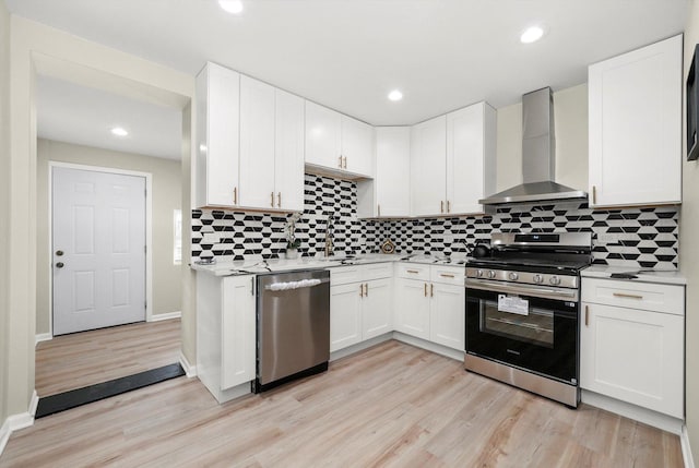 kitchen featuring appliances with stainless steel finishes, white cabinetry, light hardwood / wood-style flooring, and wall chimney range hood