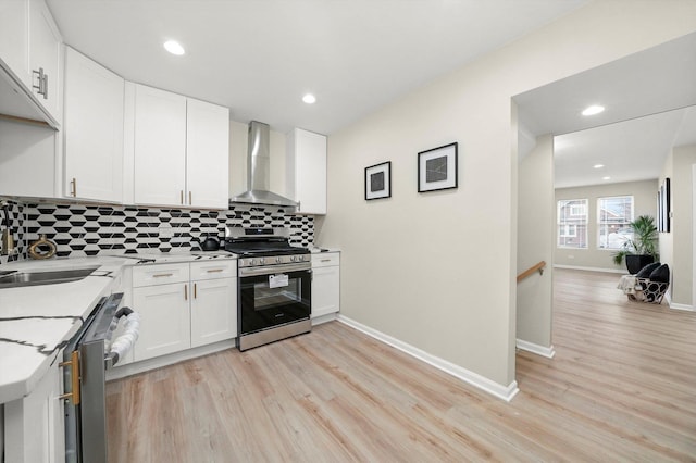 kitchen with sink, stainless steel appliances, wall chimney range hood, light hardwood / wood-style floors, and white cabinets