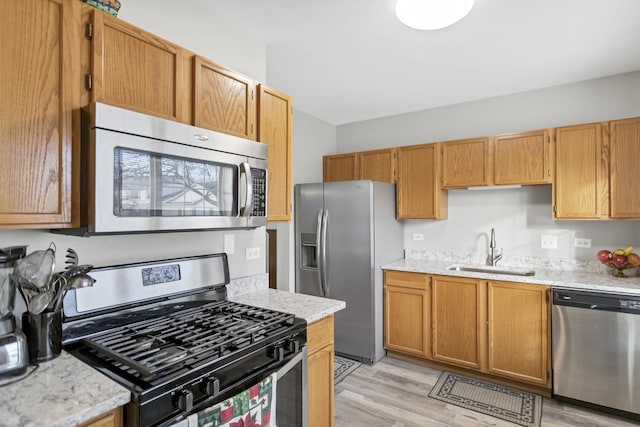 kitchen with light stone counters, sink, light hardwood / wood-style flooring, and appliances with stainless steel finishes