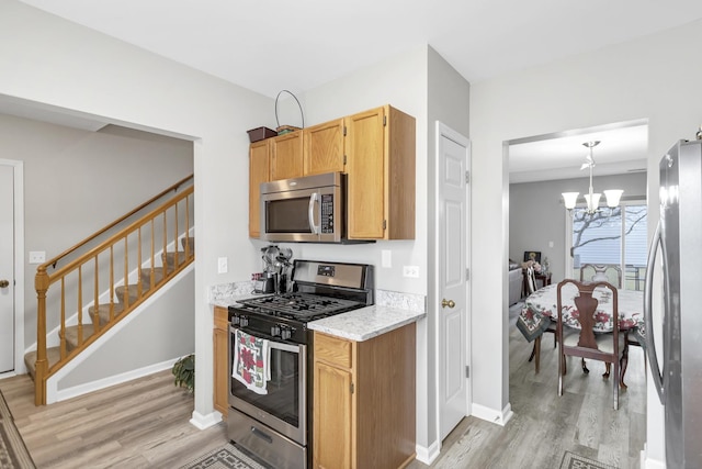 kitchen with stainless steel appliances, light hardwood / wood-style flooring, hanging light fixtures, and a notable chandelier