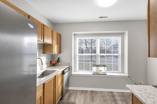 kitchen with light hardwood / wood-style floors, light stone countertops, sink, and appliances with stainless steel finishes