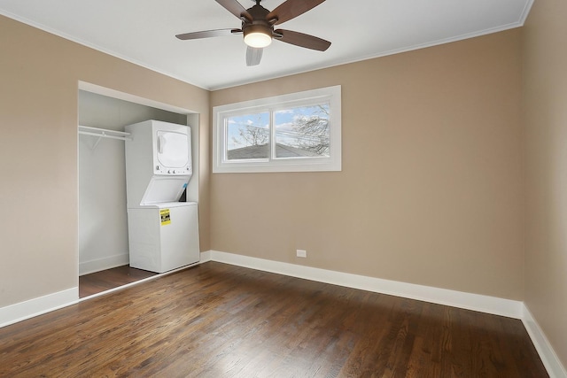 washroom featuring ceiling fan, ornamental molding, stacked washer / dryer, and dark wood-type flooring