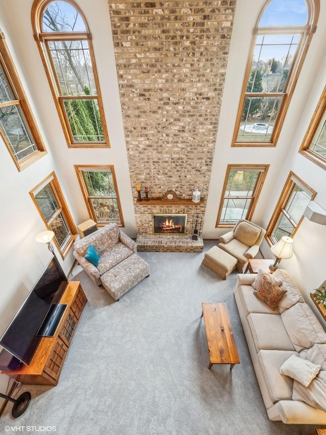 living room featuring a stone fireplace, a wealth of natural light, carpet, and a high ceiling