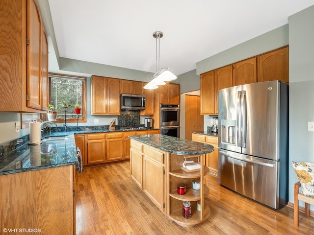 kitchen with appliances with stainless steel finishes, light wood-type flooring, dark stone countertops, a center island, and hanging light fixtures