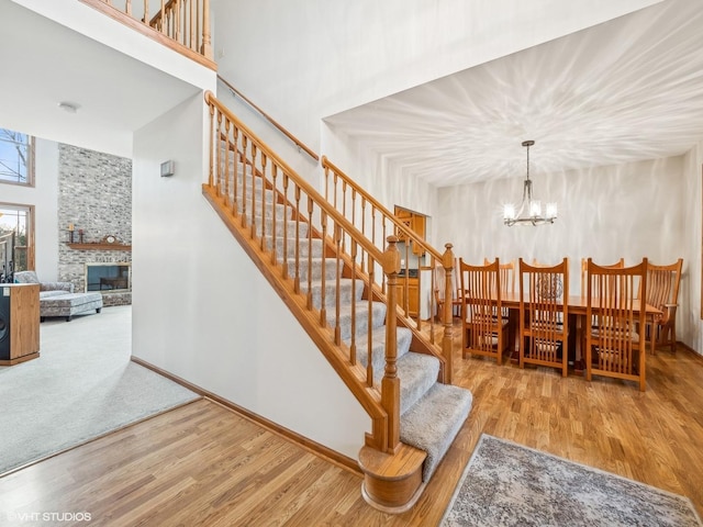 stairs featuring a chandelier, a towering ceiling, hardwood / wood-style flooring, and a stone fireplace