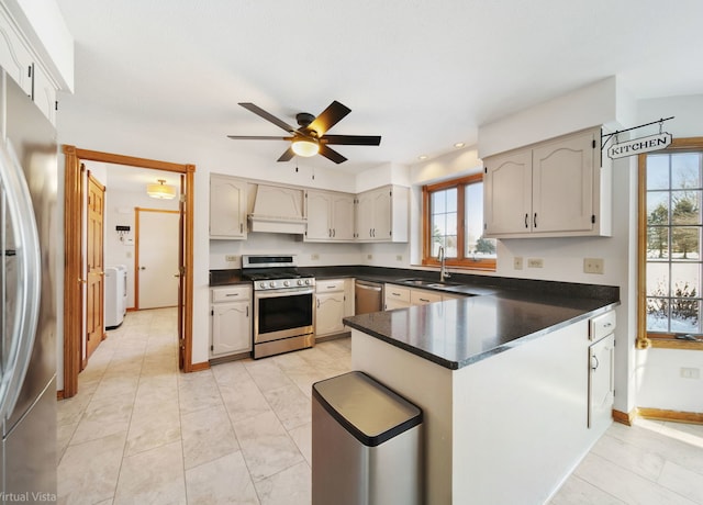 kitchen with stainless steel appliances, sink, custom range hood, ceiling fan, and washer / dryer