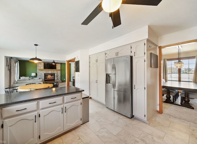 kitchen featuring pendant lighting, stainless steel refrigerator with ice dispenser, white cabinetry, ceiling fan with notable chandelier, and a stone fireplace