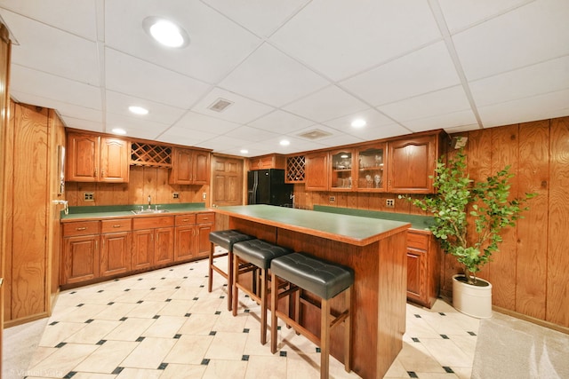 kitchen with a kitchen breakfast bar, black refrigerator with ice dispenser, a center island, and a drop ceiling