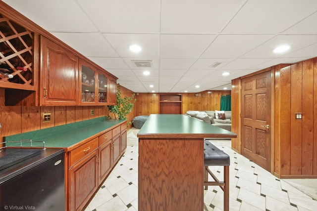 kitchen featuring a paneled ceiling, a center island, wooden walls, and a breakfast bar area