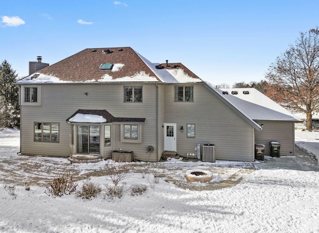 snow covered rear of property featuring a fire pit and central air condition unit