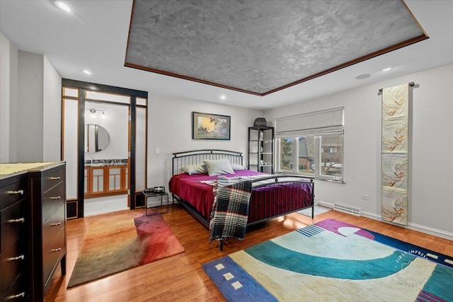 bedroom with a raised ceiling, ensuite bath, and wood-type flooring