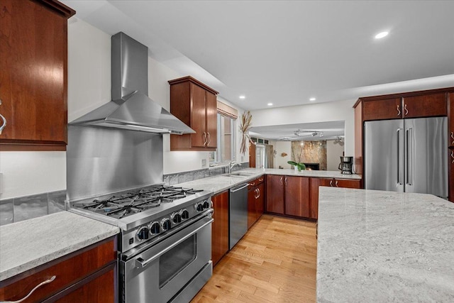 kitchen with light hardwood / wood-style flooring, wall chimney range hood, appliances with stainless steel finishes, ceiling fan, and sink