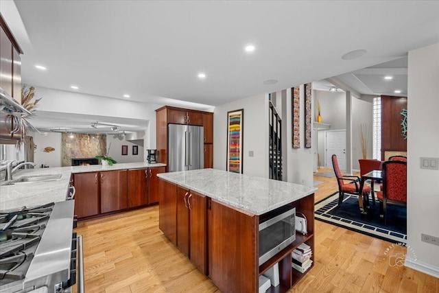 kitchen with a large fireplace, appliances with stainless steel finishes, light wood-type flooring, a center island, and sink