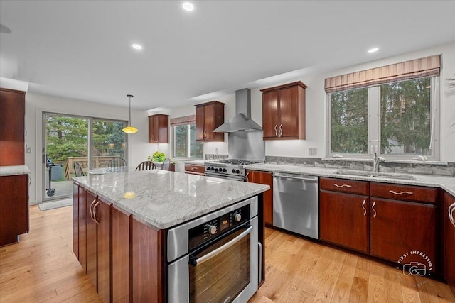 kitchen with appliances with stainless steel finishes, a center island, sink, wall chimney range hood, and decorative light fixtures