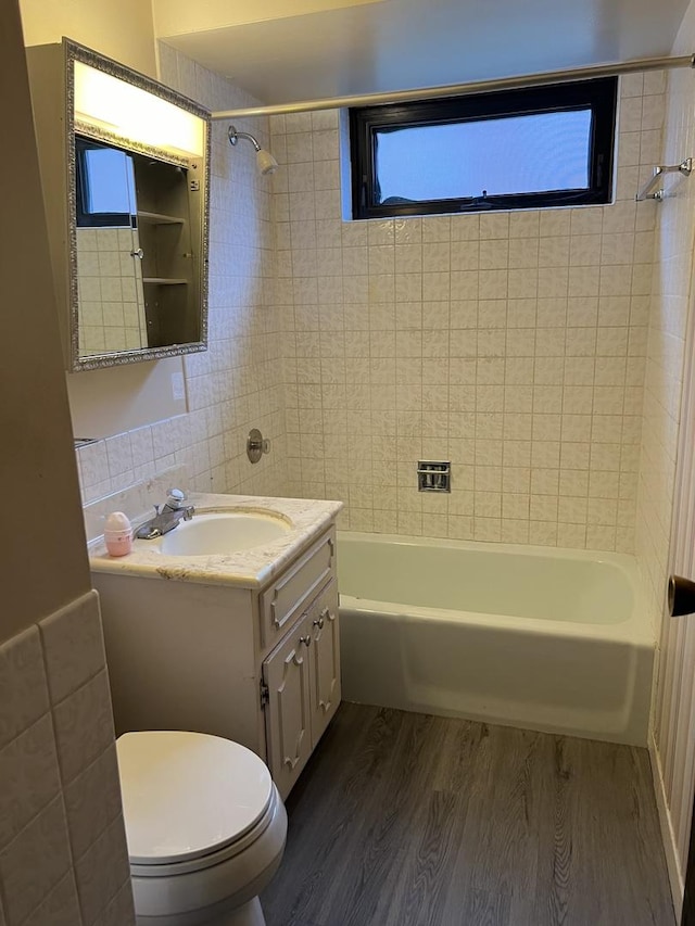 full bathroom featuring wood-type flooring, toilet, vanity, tile walls, and tiled shower / bath