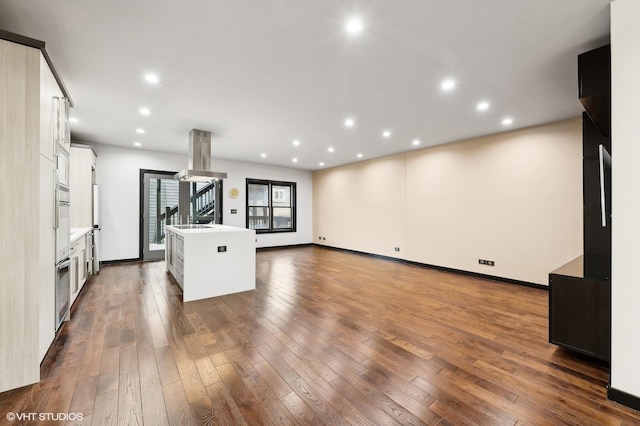 interior space with island exhaust hood, dark hardwood / wood-style floors, white cabinetry, and an island with sink