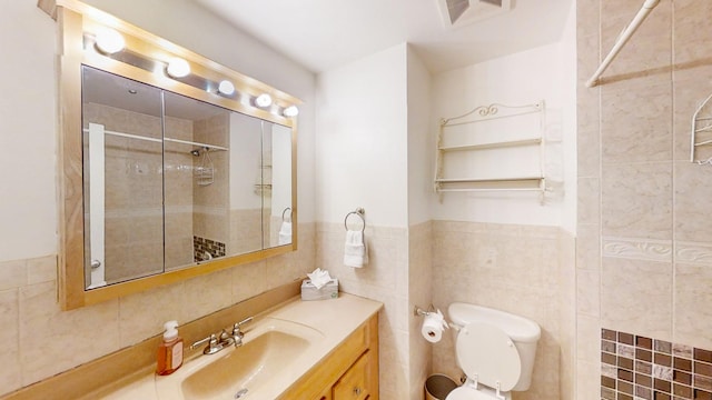 bathroom featuring toilet, a tile shower, tile walls, and vanity