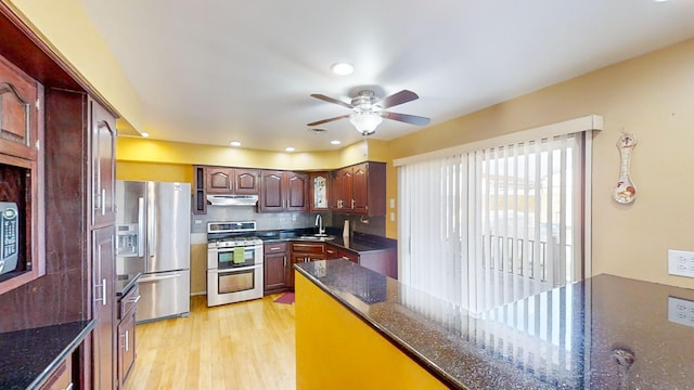 kitchen with dark stone counters, sink, light hardwood / wood-style flooring, ceiling fan, and stainless steel appliances