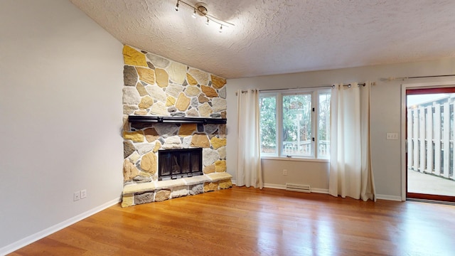 unfurnished living room with a stone fireplace, a textured ceiling, and hardwood / wood-style flooring