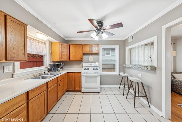 kitchen with ceiling fan, sink, gas range gas stove, light tile patterned flooring, and ornamental molding